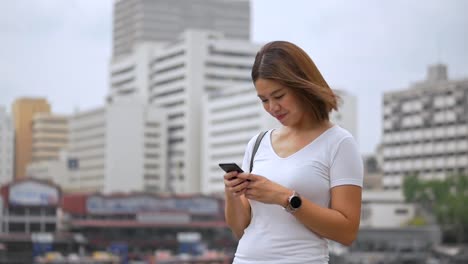 Young-asian-woman-using-smartphone-enjoying-reading-social-media-beside-fence-at-river.