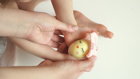 Women's-and-children's-hands-hold-chicken-egg-decorated-for-Easter-chick-with-painted-muzzle-with-eyes-and-beak-and-bow.