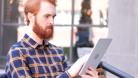 Bart-junge-Mann-mit-Tablet-beim-Sitzen-im-Freien