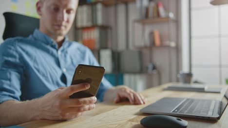 Businessman-Sitting-at-His-Desk-Works-on-Desktop-Computer-in-the-Stylish-Office,-Picks-up-and-Starts-Using-Smartphone,-Uses-Social-Media-App,-Emailing-Business-Partners,-Messaging