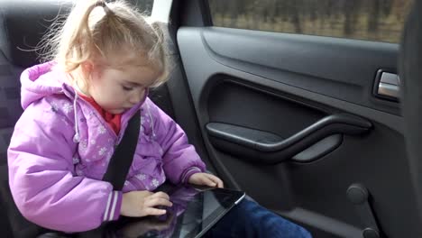 Little-girl-warm-clothing,-playing-on-your-tablet-PC-in-car