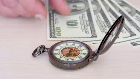 Time-is-money---a-pocket-watch-on-a-background-of-one-hundred-dollar-bills