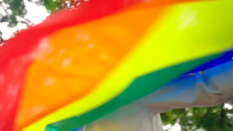 Glückliche-junge-asiatische-Tomboy-Mädchen-tanzen-und-winken-Regenbogen-LGBT-Flagge-im-Park,-Zeitlupe