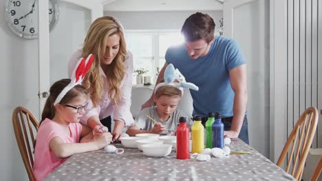 Familie-sitzt-um-Küchentisch-mit-Eltern,-die-Kindern-helfen,-Eier-für-Ostern-zu-malen---in-Zeitlupe-gedreht