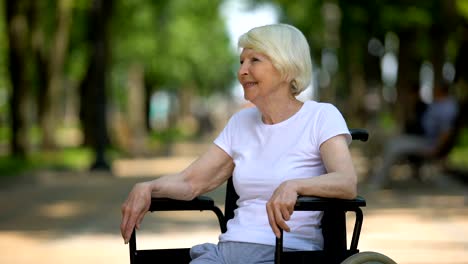 Happy-elderly-female-in-wheelchair-enjoying-sunny-day-in-park,-rehabilitation