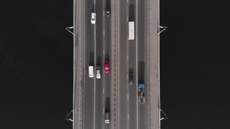 Bridge-highway-dark-water-red-car-in-traffic-aerial-top-view