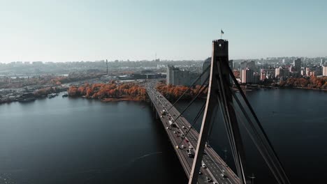 Ukrainische-Flagge-weht-auf-Brücke-verbindet-zwei-Ufer-der-Metropole.-Luft-Drohnenansicht-der-Betonbrücke-mit-viel-Befahrenem-Autoverkehr.-Flug-einer-Drohne-über-Brücke-mit-schönem-Stadtbild-mit-Fluss.-Kiew,-Ukraine