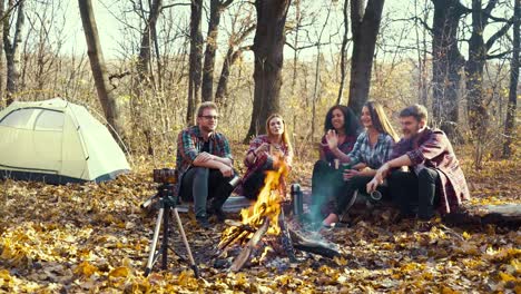 Travelers-sitting-by-campfire-and-live-streaming-using-smartphone-on-tripod