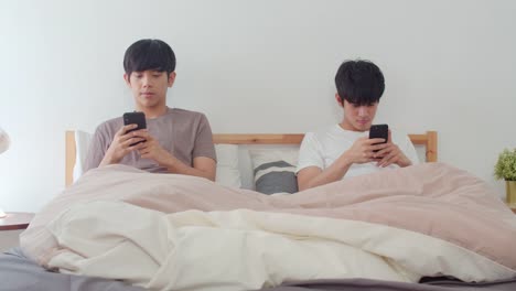 Pareja-gay-asiática-usando-el-teléfono-móvil-en-casa.-Jóvenes-hombres-LGBTQ-asiáticos-feliz-descanso-juntos-después-de-despertar,-comprobar-las-redes-sociales-acostado-en-la-cama-en-el-dormitorio-en-casa-en-el-concepto-de-la-mañana.-Disparo-a-cámar