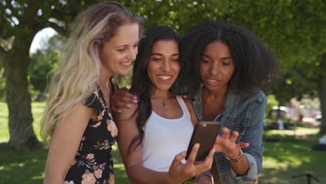 Happy-young-group-of-multi-ethnic-female-friends-browsing-using-smartphone-technology-enjoying-sharing-moments-with-each-other-in-the-park-on-a-sunny-day