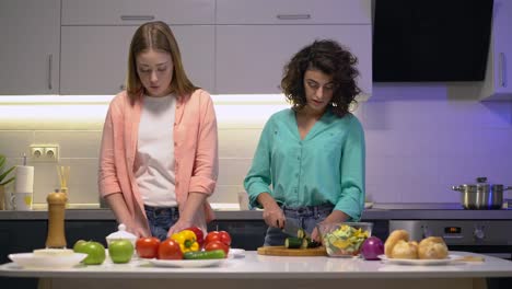 Young-pretty-females-talking-in-kitchen,-preparing-vegetable-meal,-communication