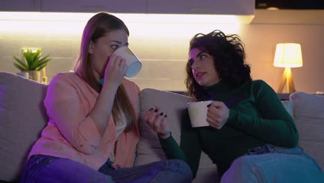 Female-couple-with-cups-of-hot-beverage-talking-in-cozy-atmosphere-romantic-date