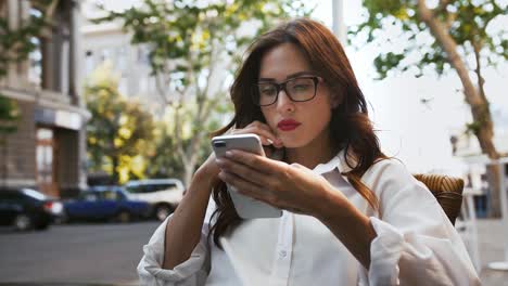 Business-female-in-glasses,-white-shirt.-She-feeling-disappointed-and-shocked-reading-news-using-cellphone,-sitting-in-roadside-cafe.-Slow-motion