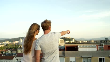 CLOSE-UP:-Liebhaber-stehen-auf-Dachterrasse-Blick-auf-atemberaubende-Stadt-zeigenden-Finger