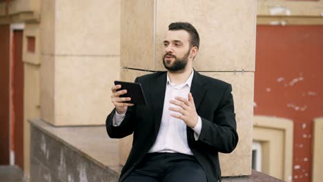 Joven-barbudo-hombre-de-negocios-hablando-en-la-tableta-de-tener-reunión-de-negocios-de-chat-de-vídeo.-Empresario-usando-aplicación-para-tener-una-conversación-de-videoconferencia