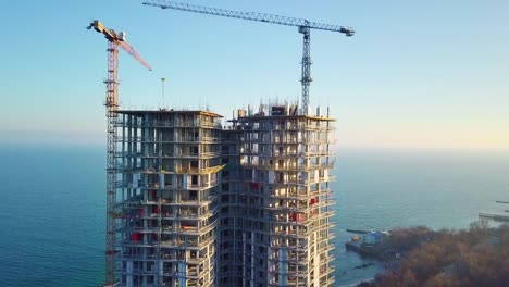 Aerial-city-view.-Construction-of-a-high-rise-skyscraper-on-the-ocean-by-two-cranes.-Even-slow-travel