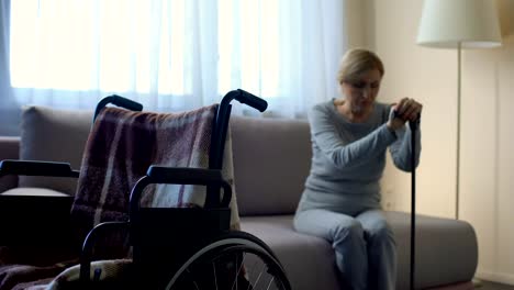 Lonely-disabled-woman-sitting-on-sofa-and-looking-at-empty-wheelchair,-memories