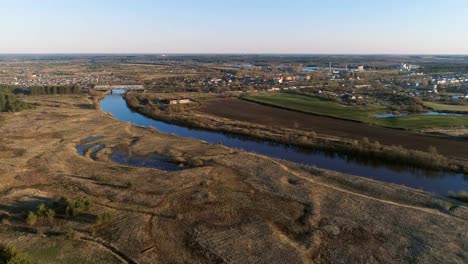 Flight-above-green-fields,-forest,-river-and-village-early-spring,-aerial-panoramic-view.