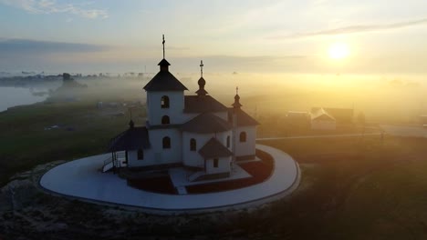 Luftaufnahmen-Video-der-kleinen-Dorfkirche-am-nebligen-Morgen.-Sonnenaufgangszeit.-Kyiv-Region,-Ukraine.-Fliegen-über-den-Fluss-Desna