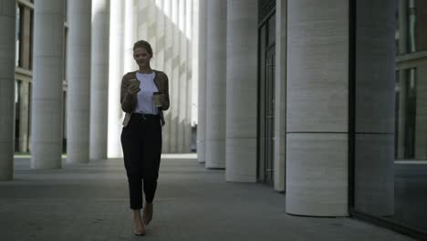 Smiling-young-woman-walking-in-high-heels-and-enjoying-text-messaging-on-her-smartphone-in-slow-motion