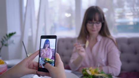 nutrición-adecuada,-sonriente-a-chica-de-gafas-posando-con-la-placa-de-la-fruta-para-novia-que-toma-foto-en-el-celular,-sentado-en-la-mesa-de-café