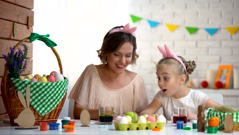 Little-girl-excitedly-watching-mother-dipping-egg-in-green-food-coloring,-Easter