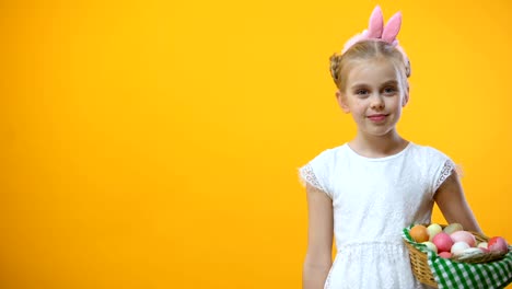 Female-child-in-bunny-ears-headband-holding-Easter-basket-and-showing-thumbs-up