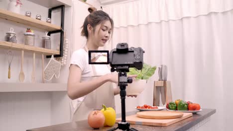 Mujer-asiática-blogger-usando-cámara-de-grabación-cómo-hacer-comida-sana-ensalada-video-para-su-abonado,-verduras-orgánicas-de-uso-femenino-preparar-ensalada-para-cuerpo-en-forma-en-casa.-Concepto-de-comida-sana.