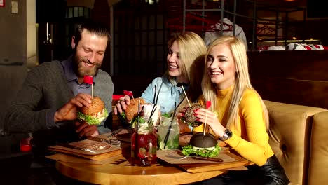 Happy-friends-are-eating-burgers,-talking-and-smiling-in-a-cafe.