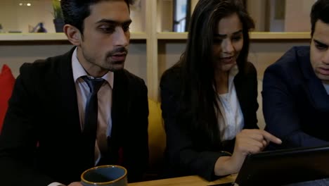 Handheld-shot-of-coworkers-colleagues-huddled-together-at-cafe-table-as-they-stare-at-laptop-screen-coming-up-with-solution