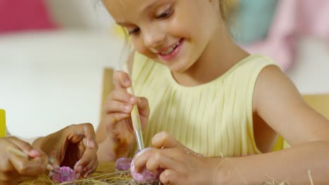 Linda-niñita-sonriendo-y-poniendo-brillo-en-huevo-de-Pascua