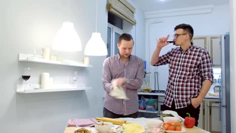 Un-par-de-hombres-gays-coquetan-entre-sí-cocinando-una-pizza-juntos-y-bebiendo-un-vino.