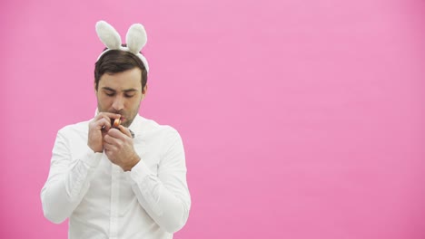 Young-handsome-boy-standing-on-a-pink-background.-A-man-with-rabble-ears-on-his-head.-A-man-holding-a-carrot-puts-it-in-his-mouth-and-wants-to-light-an-ashtray.-Throws-carrots-and-taking-a-cigar-lit-it.