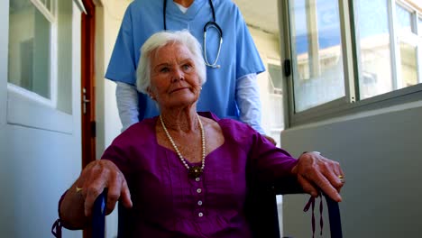 Vista-frontal-de-mujer-caucásica-médico-empujando-paciente-Senior-en-silla-de-ruedas-en-casa-de-ancianos-4k