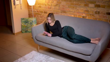 Closeup-top-shoot-portrait-of-young-relaxed-woman-using-the-phone-and-lying-on-the-couch-resting-indoors-at-cozy-home