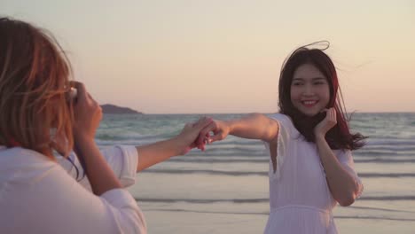 Young-Asian-lesbian-couple-using-camera-taking-photo-each-other-near-beach.-Beautiful-women-lgbt-couple-happy-romantic-moment-when-sunset-in-evening.-Lifestyle-lesbian-couple-travel-on-beach-concept.