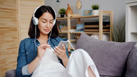 Beautiful-young-woman-listening-to-music-through-headphones-using-smartphone