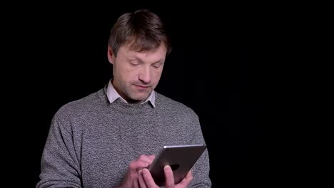 Closeup-shoot-of-adult-caucasian-man-messaging-on-the-tablet-in-the-front-of-camera-with-backround-isolated-on-black