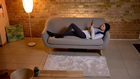 Nahaufnahme-von-jungen-hübschen-kaukasischen-Hipster-Weiblich-mit-dem-Tablet,-während-auf-dem-Sofa-in-einer-gemütlichen-Wohnung-liegen