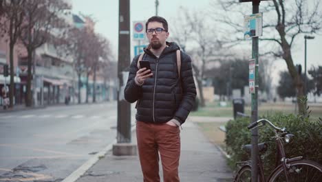 El-hombre-está-esperando-el-autobús-en-la-estación-y-el-uso-de-teléfono-inteligente