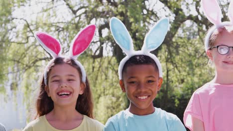 Portrait-of-group-of-children-wearing-bunny-ears-on-Easter-egg-hunt-in-garden-smiling-at-camera---shot-in-slow-motion