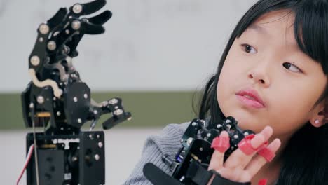 Little-Girl-is-playing-with-robotic-arm-in-a-school.-She-is-controlling-it-by-her-hand.