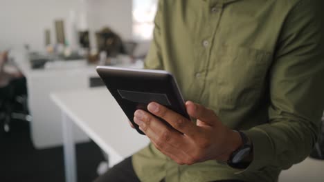 Nahaufnahme-des-jungen-Geschäftsmannes-im-Hemd-sitzt-auf-weißem-Schreibtisch-mit-digitalen-Tablet-in-modernen-Büro-sitzen