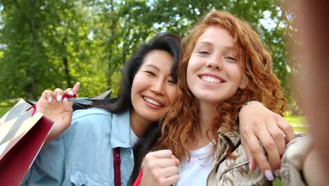 Attraktive-Damen-machen-Selfie-im-Park-mit-Einkaufstaschen-Blick-auf-die-Kamera