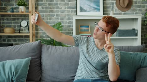 Joyful-teenager-taking-selfie-with-smartphone-camera-posing-on-couch-at-home