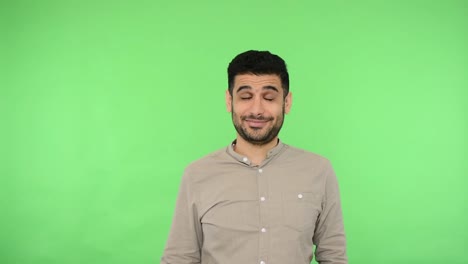 Positive-smiling-handsome-man-with-bristle-in-shirt-standing-with-embarrassed-expression-and-holding-social-media-heart-Like-icon.-green-background