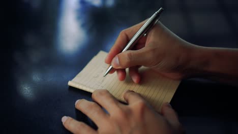 4K-Video-Kopie-Raum-des-Mannes-Hand-schreiben-in-weißen-Notizbuch-mit-Bokeh-Licht-im-Café-Hintergrund.