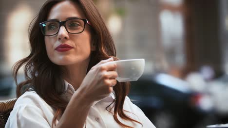 Business-Lady-in-Brille-und-weißem-Hemd.-Sie-sitzt-am-Tisch-im-Café-im-Freien.-Lesen-Sie-Nachrichten-auf-dem-Handy-und-Kaffee-trinken.-Nahaufnahme