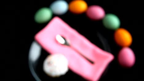 On-black-table-lay-different-colored-eggs,-Easter-cake,-plate-spoon,-and-napkin.