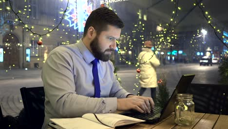 Konzentrierte-sich-Geschäftsmann-Arbeit-mit-Laptop-und-Notizen,-Café,-Abend,-Weihnachten